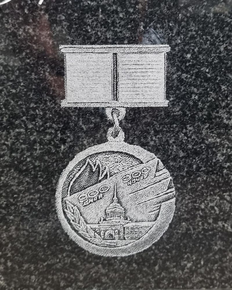 Крупный план гравировки юбилейной медали с колодкой в память 300-летия Санкт-Петербурга на чёрном крапчатом граните