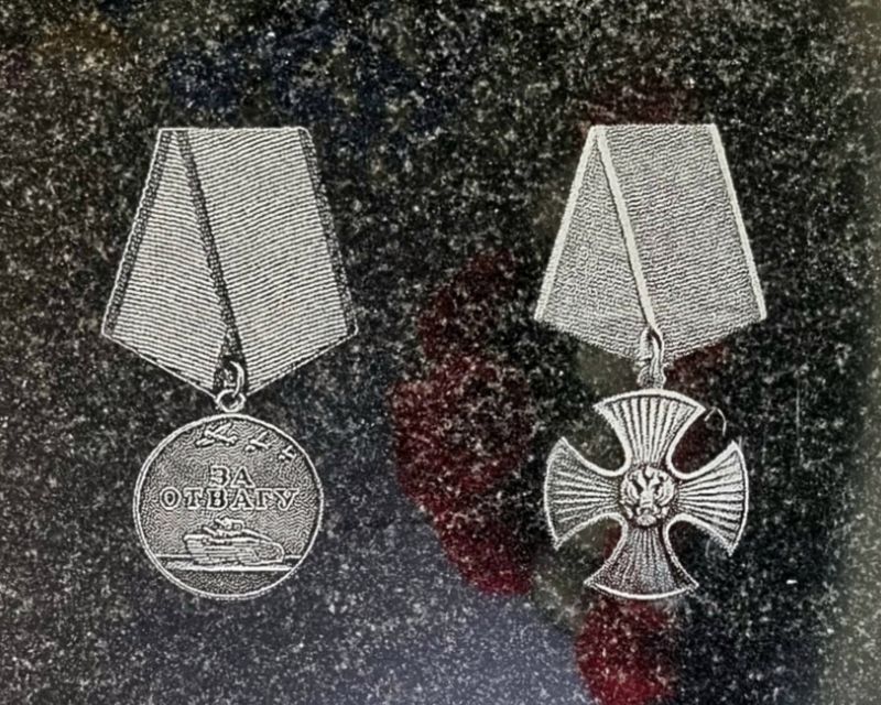 крупный план гравировки двух наград рядом: медаль «За отвагу» и орден Мужества на чёрном граните