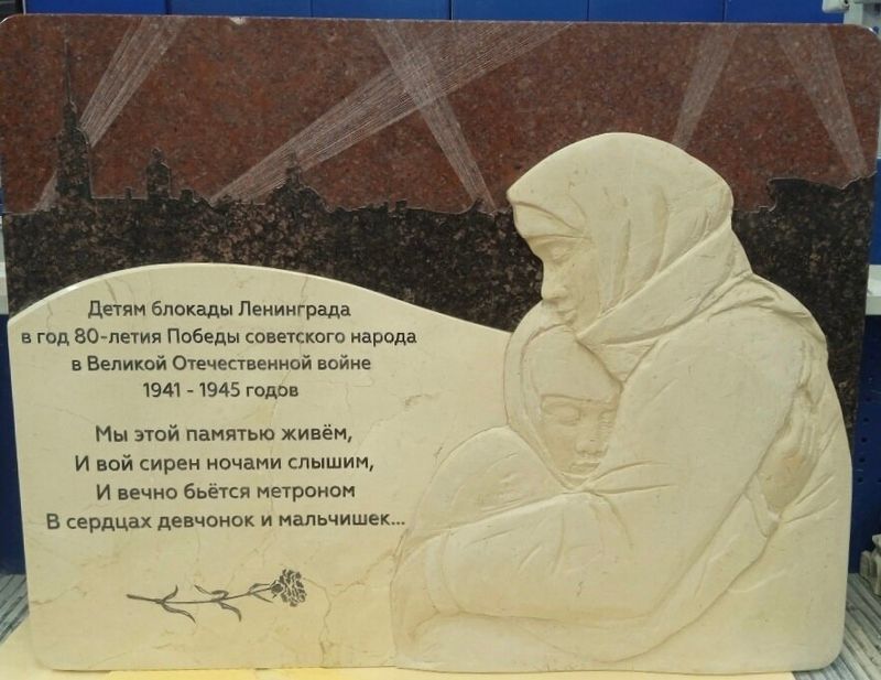 Горизонтальная плита из красно-коричневого гранита с объёмным светлым барельефом женщины с ребёнком и посвящением детям блокады Ленинграда