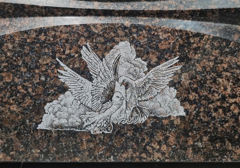 Полированный коричневый гранит с фаской по верхнему краю, гравировка голубей на облаке